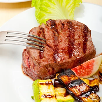 A filet mignon on a plate with fork and other vegetables