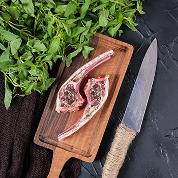 Two slices of raw beef with a knife and leafy vegetable on the side