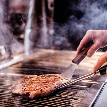 A chef cooking a steak on a grill