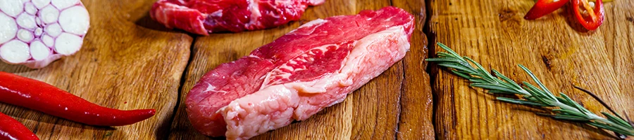 A raw steak on a wooden table with other ingredients at the sides