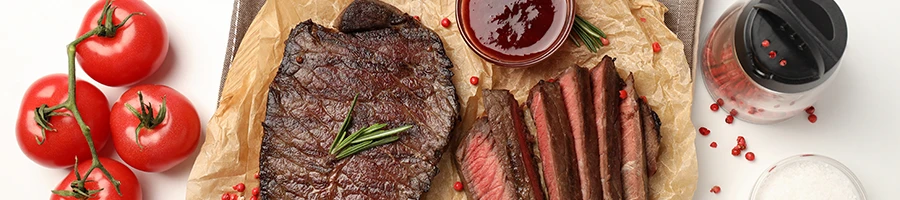 A roast beef with tomatoes and sauce on a chopping board