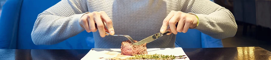 A person holding a knife and fork while eating steak