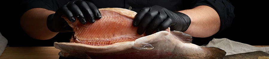 A man wearing a gloves holding a sliced fish