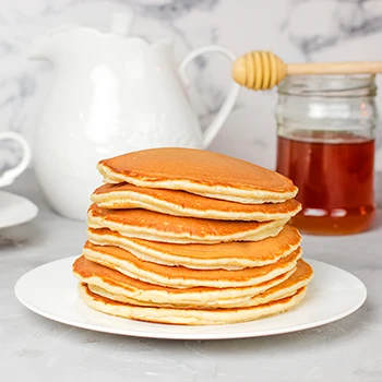 A stack of pancakes on a plate with a jar of honey behind