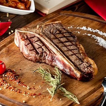 A T-bone steak on a cutting board with different spices on the side
