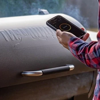 A person using a phone in front of a smoker grill