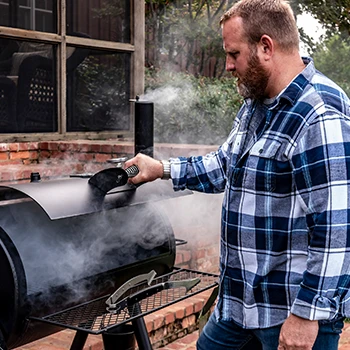 A person opening the lid of an offset smoker