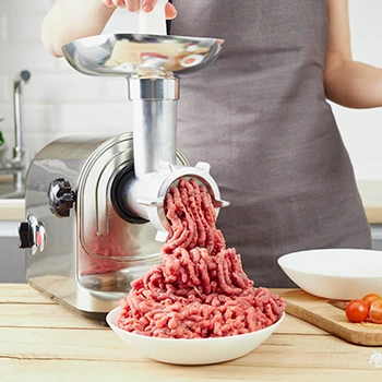 A woman wearing an apron using a meat grinder