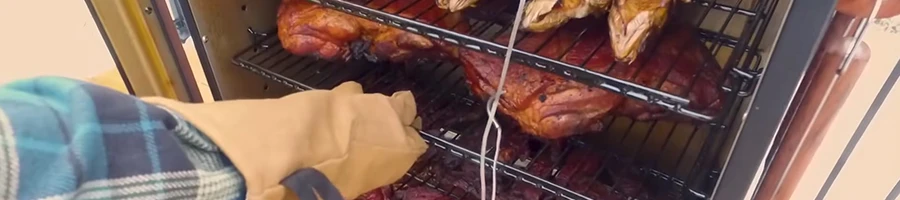 A person inserting meat in a vertical smoker while wearing mittens