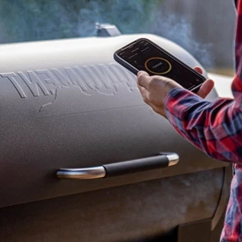 A person using mobile phone in front of a smoker grill