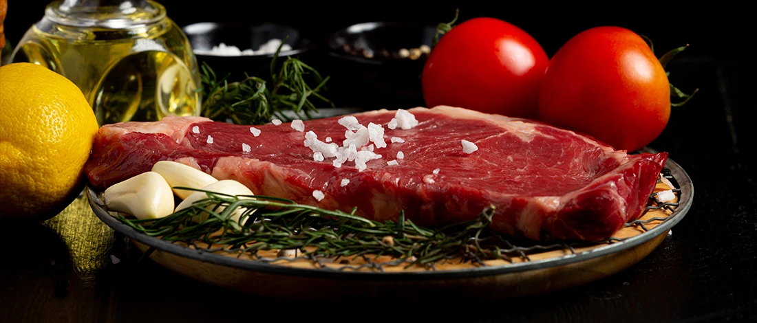 An image of raw meat with salt on top and other ingredients on the side
