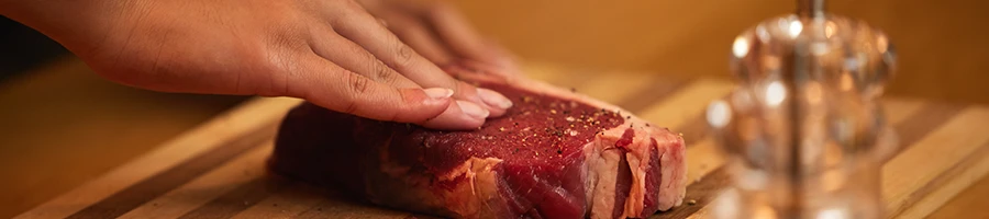 A person preparing a steak on a cutting board