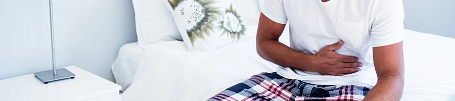 A man holding his stomach while sitting on a bed