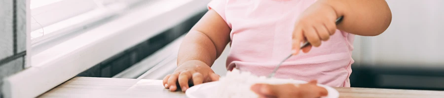 A close up image of a baby sitting in front of a table while eating