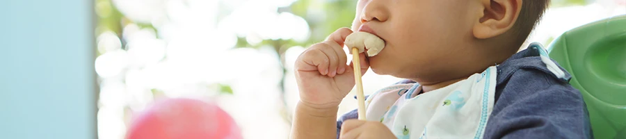 An image of sitting baby while eating all by himself