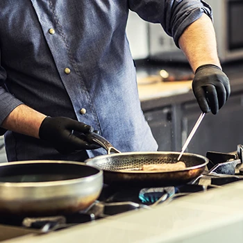 An image of a chef cooking who is wearing black gloves