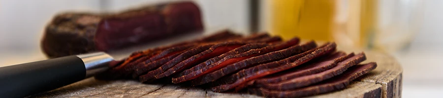 An image of pastrami slices and a knife on a cutting board