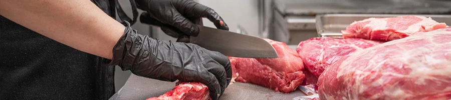 A chef wearing black gloves slicing beef meat