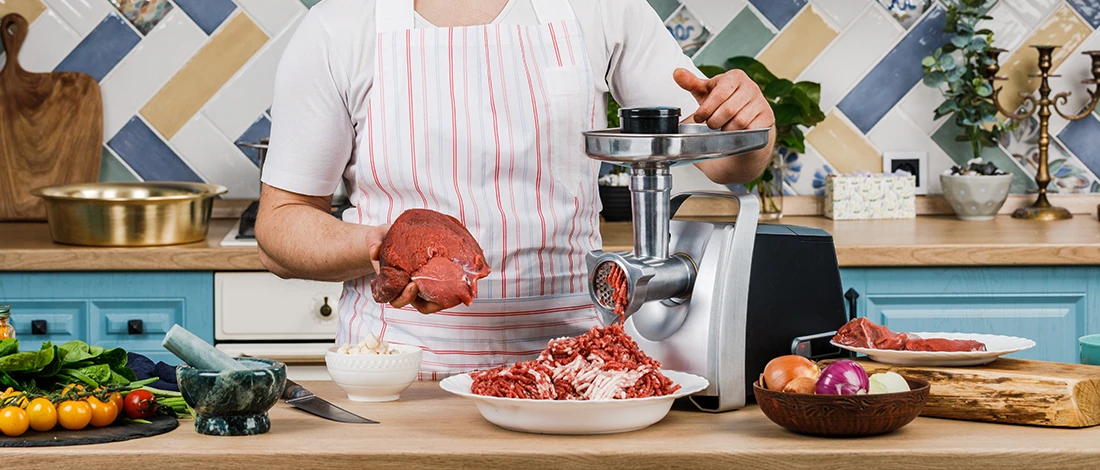 An image of a chef using meat grinder in the kitchen