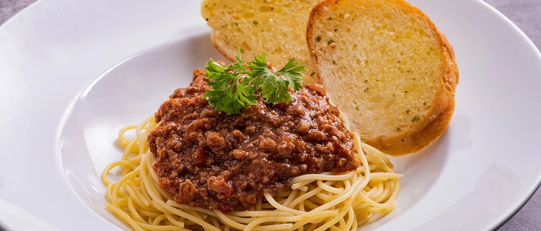 An image of spaghetti and bread on a white plate