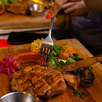 A woman slicing grilled meat on top of a chopping board