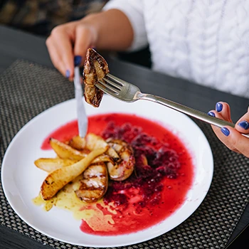A close up image of a woman eating a grilled meat in a fancy restaurant