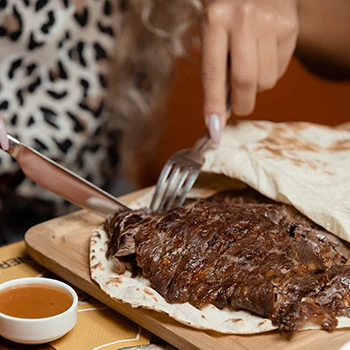 A woman slicing steak meat on top of a flat bread