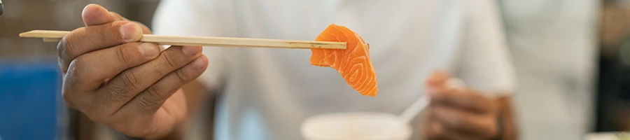 A person holding a salmon meat using chopsticks