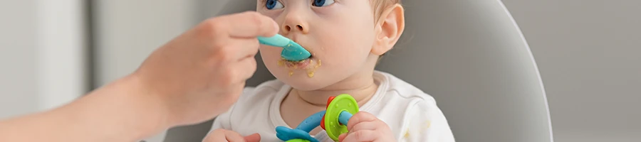 An image of a baby sitting while being fed by her mother