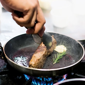 An image of a person cooking steak on a pan