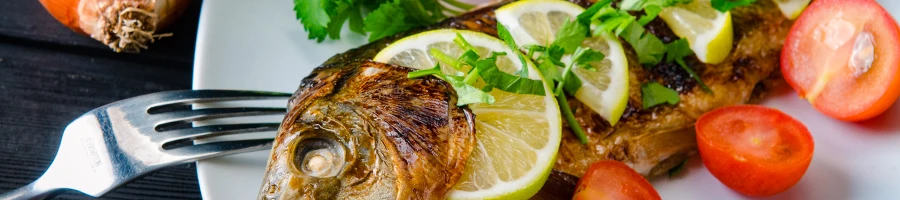 An image of cooked fish meat with different lemons and tomatoes on a plate