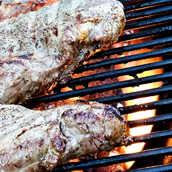 A close up image of grill grates with meat on top