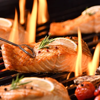 A close-up image of grilled fish on a flaming small grill