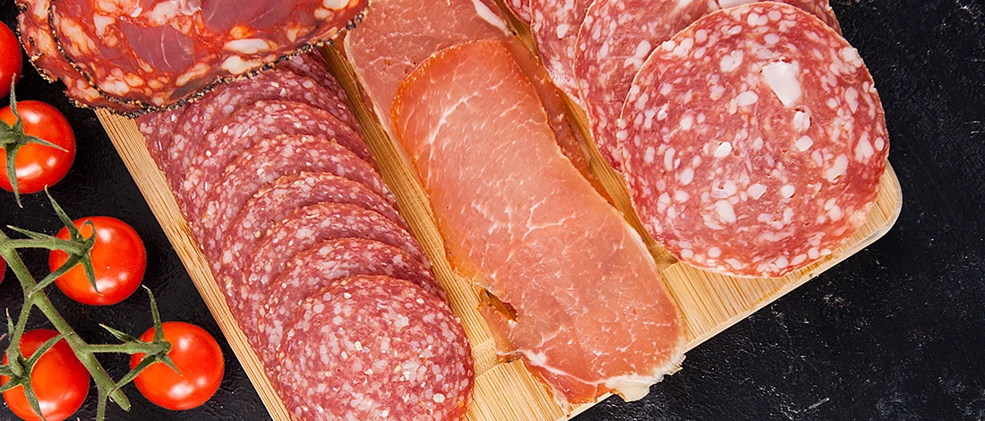A close up image of deli meats on top of a wooden board