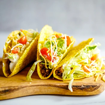 An image of three tacos on a wooden board