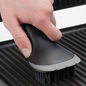 An image of a hand using a brush for cleaning an indoor grill