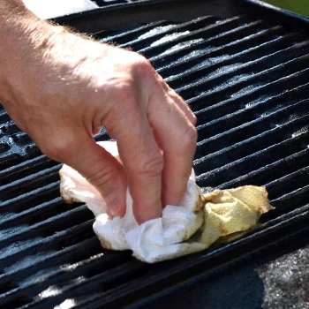 An image of a person cleaning a grill with tissue cloth