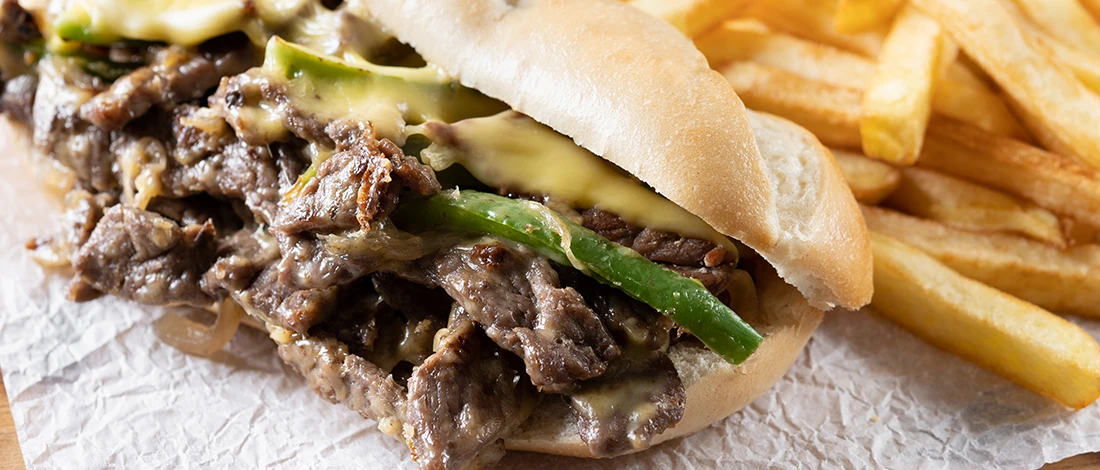 A close up image of Philly cheesesteak sandwich and a side of fries