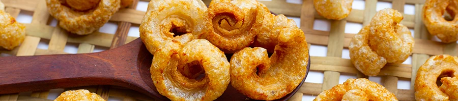 A close up image of pork rinds on a wooden spoon and a basket