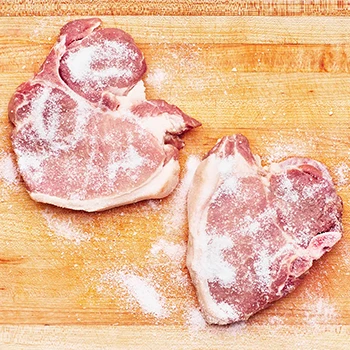 A top view image of raw meat sprinkled with sugar on a wooden board