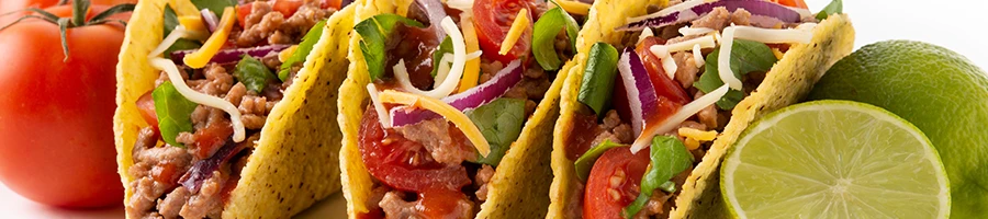A close up image of tacos with tomato and limes on the side