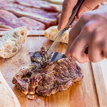 A person who is slicing meat on a cutting board