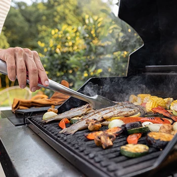 A close up image of a person placing food on a gas grill