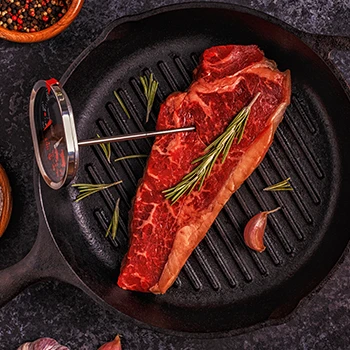 A top view image of a steak and a meat thermometer on a pan