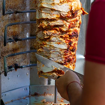 An image of a man slicing some gyro meat on a vertical rotisserie