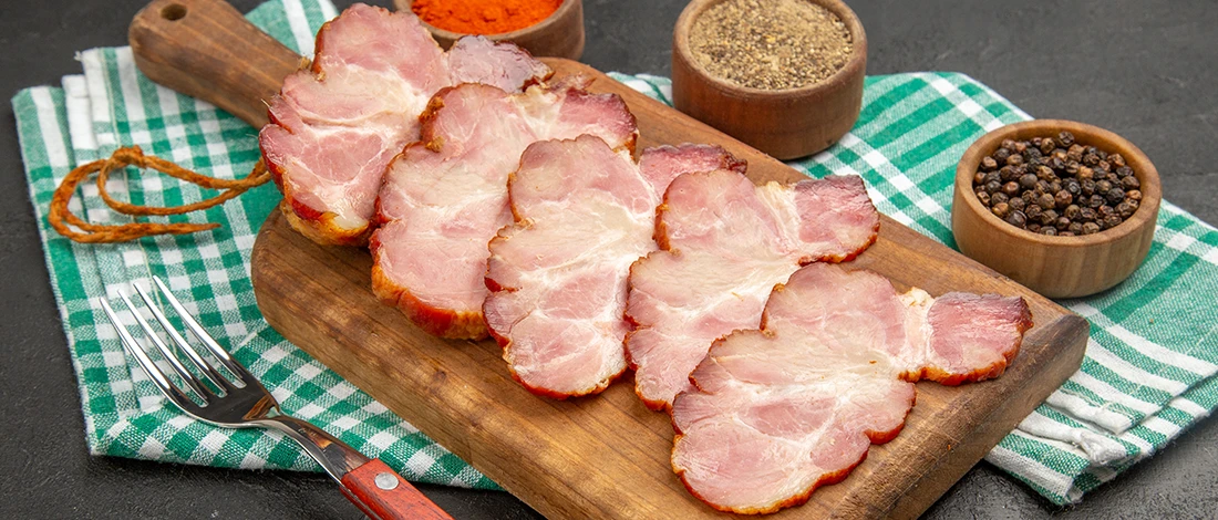 Ham slices sitting out on a wooden board with spices on the side
