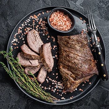 An image of cooked tri-tip steak on a black plate