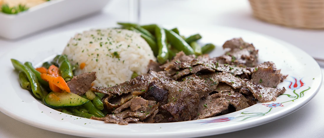 An image of gyro meat with rice on a white plate