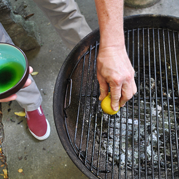 An image of a person cleaning and scrubbing a charcoal grill
