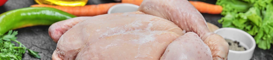 A close up shot of a whole chicken with spices and vegetable in the background